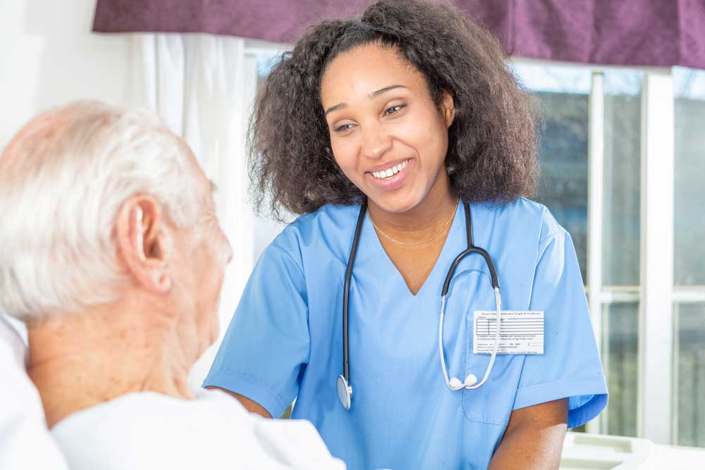 African nurse smiling to elder male patient.
