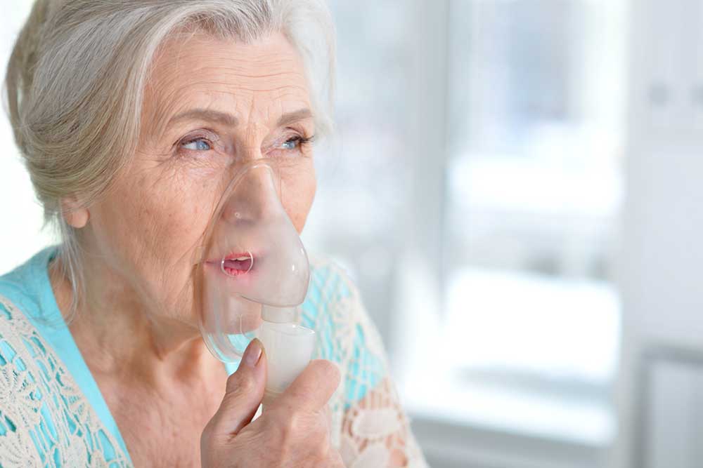 Senior woman making inhalation using machine.
